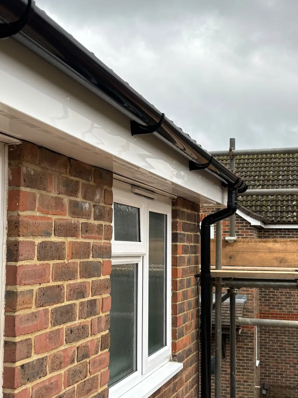 Close-up of new black gutter and downpipe on brickwork
