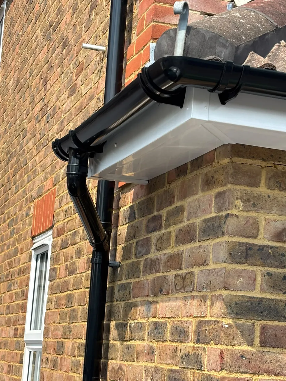 New black uPVC gutter and downpipe on a brick house corner